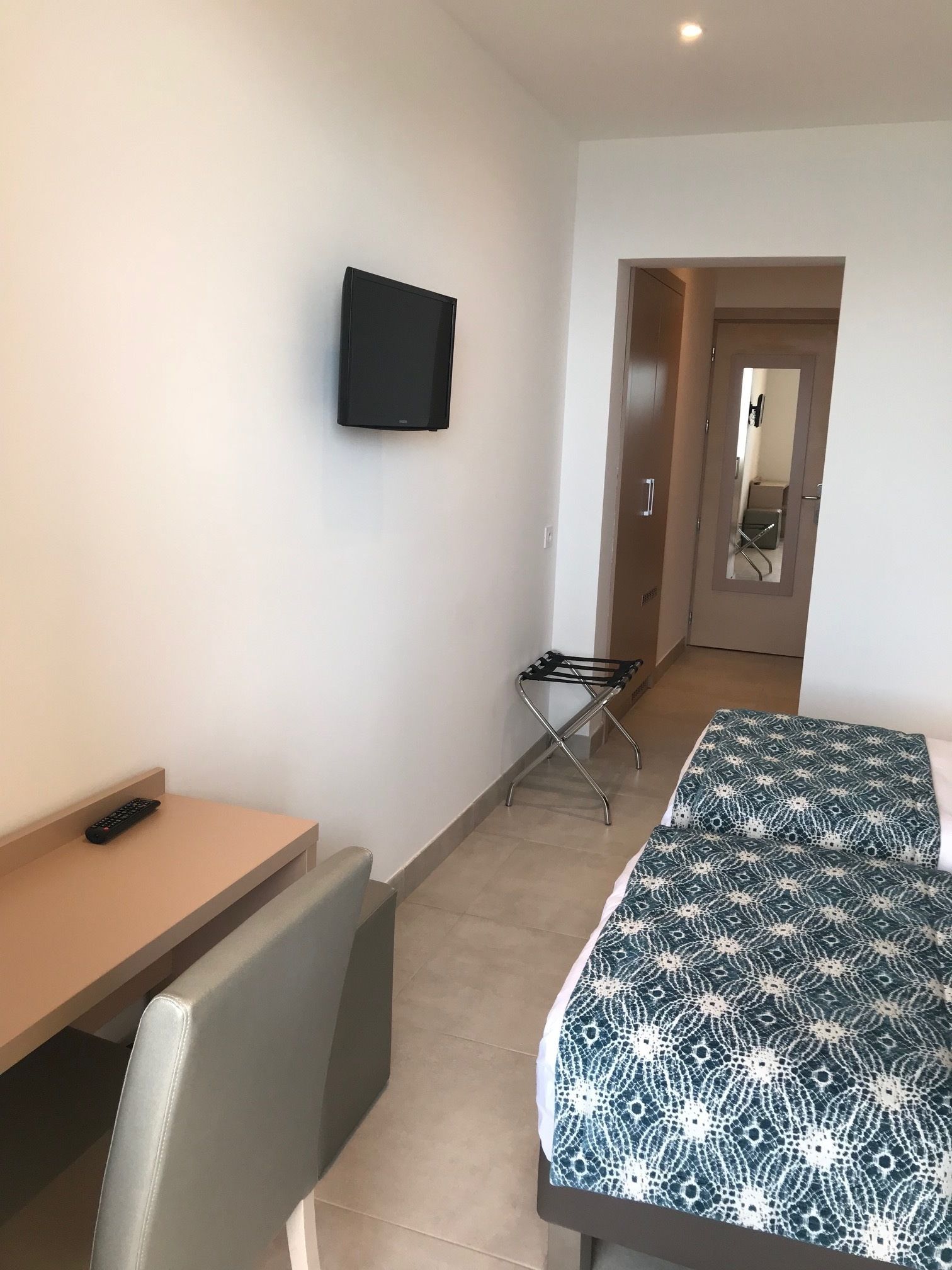 A hotel room with a bed, a TV mounted on the wall, a desk, and a chair.