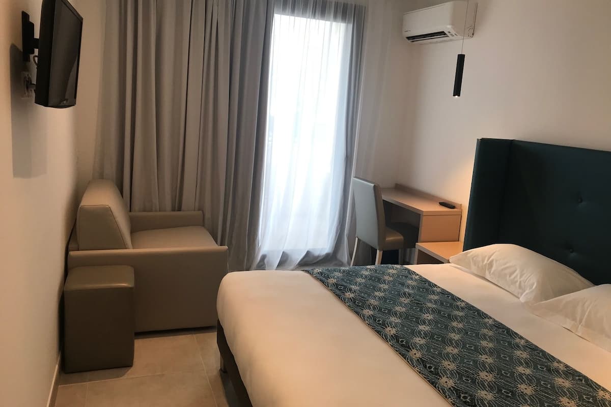 Een hotelkamer met een bed, een bureau, een stoel en een airconditioning.