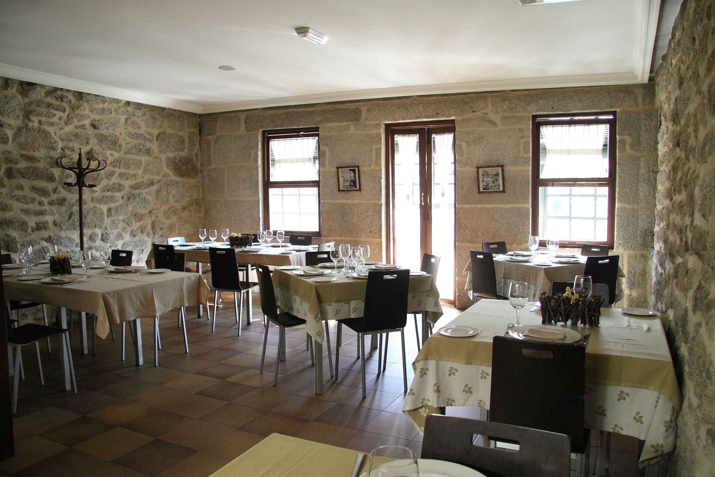 Un espace repas avec des murs en pierre, de nombreuses tables dressées et de grandes fenêtres laissant entrer la lumière naturelle.