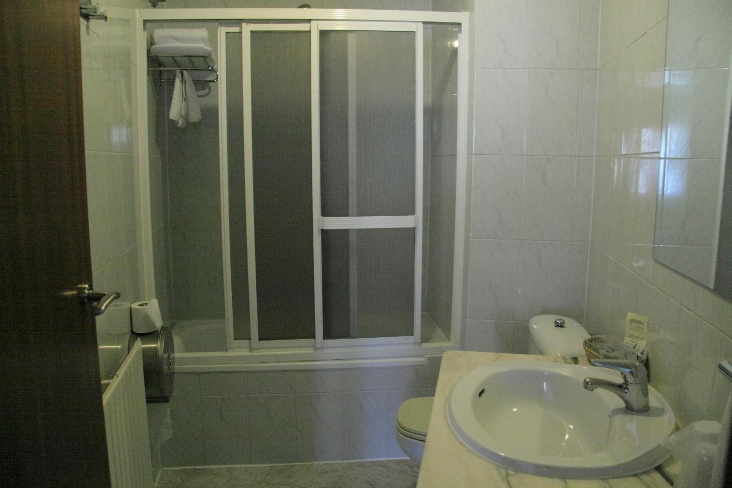 A bathroom with a shower enclosure, toilet, sink, and a towel rack.