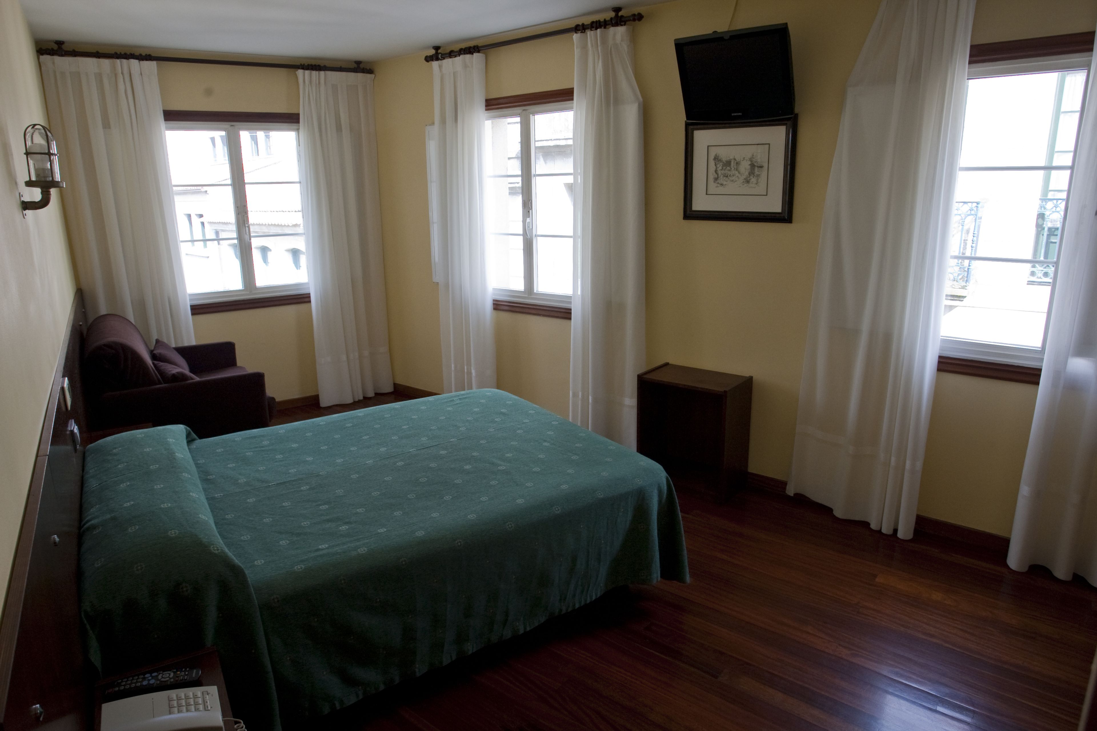 A hotel room with a bed, a small table, a chair, and a window with curtains.
