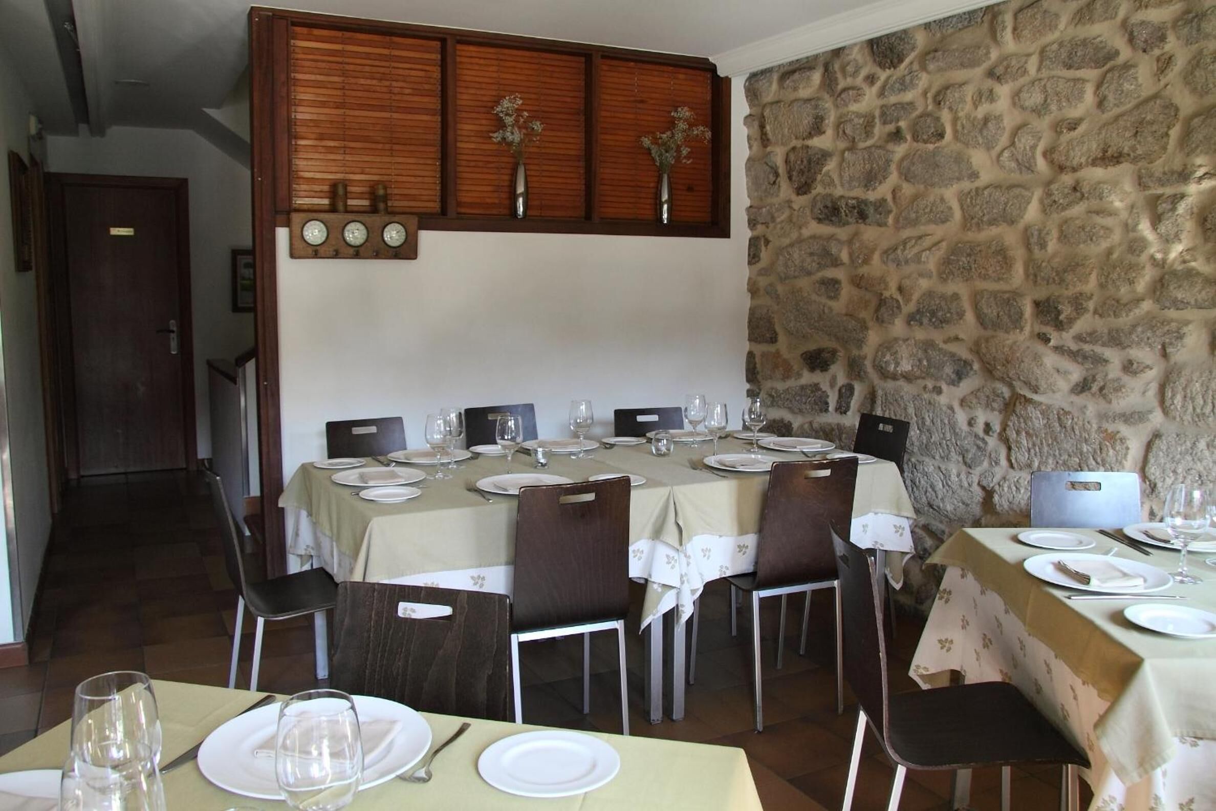 A dining area with tables set for four, stone walls, and a wooden panel above the tables.