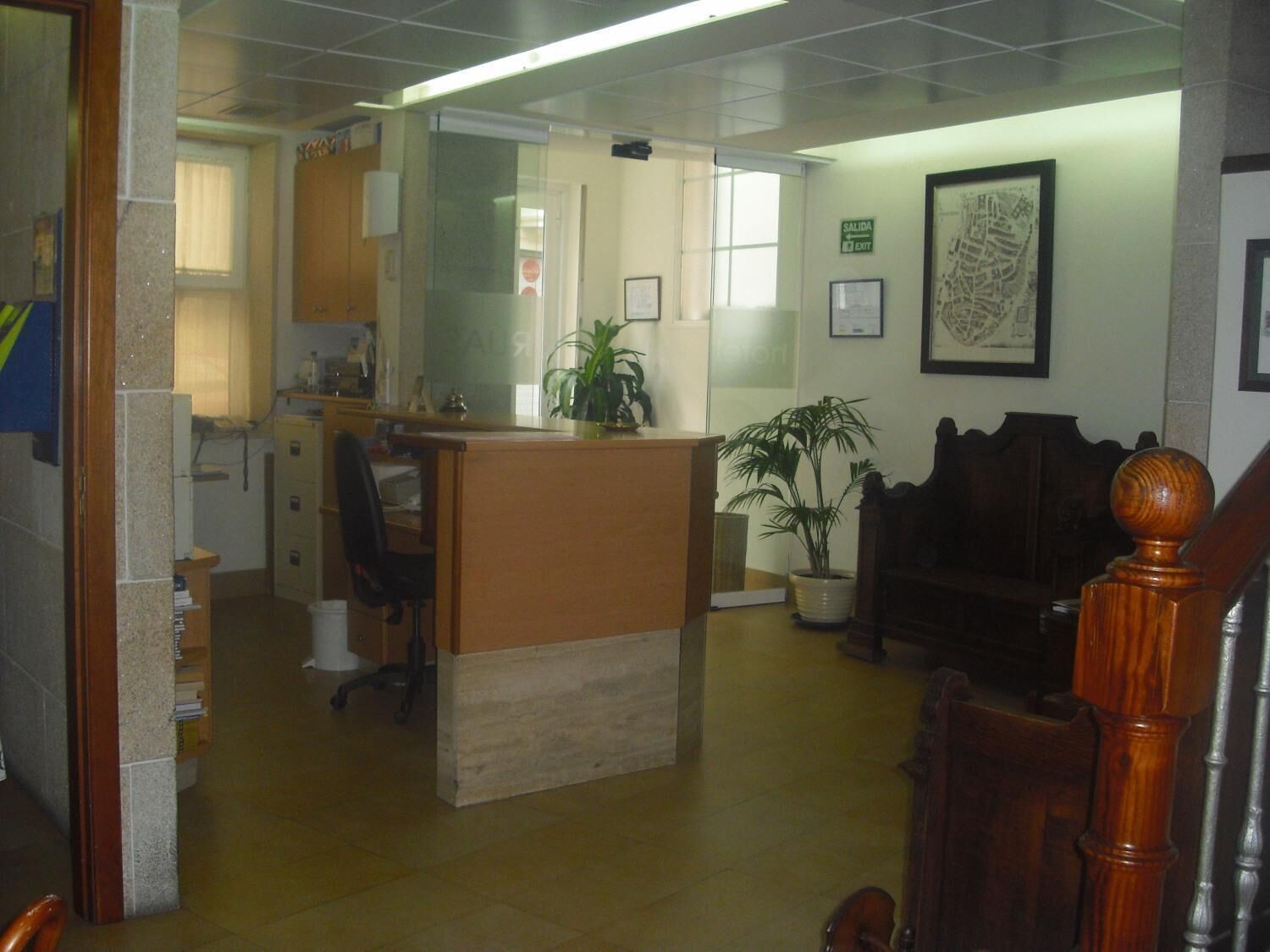 A reception area with a desk, chairs, a potted plant, and a staircase.
