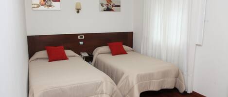 A hotel room with two beds, a wooden headboard, a nightstand, a lamp, and artwork on the walls.