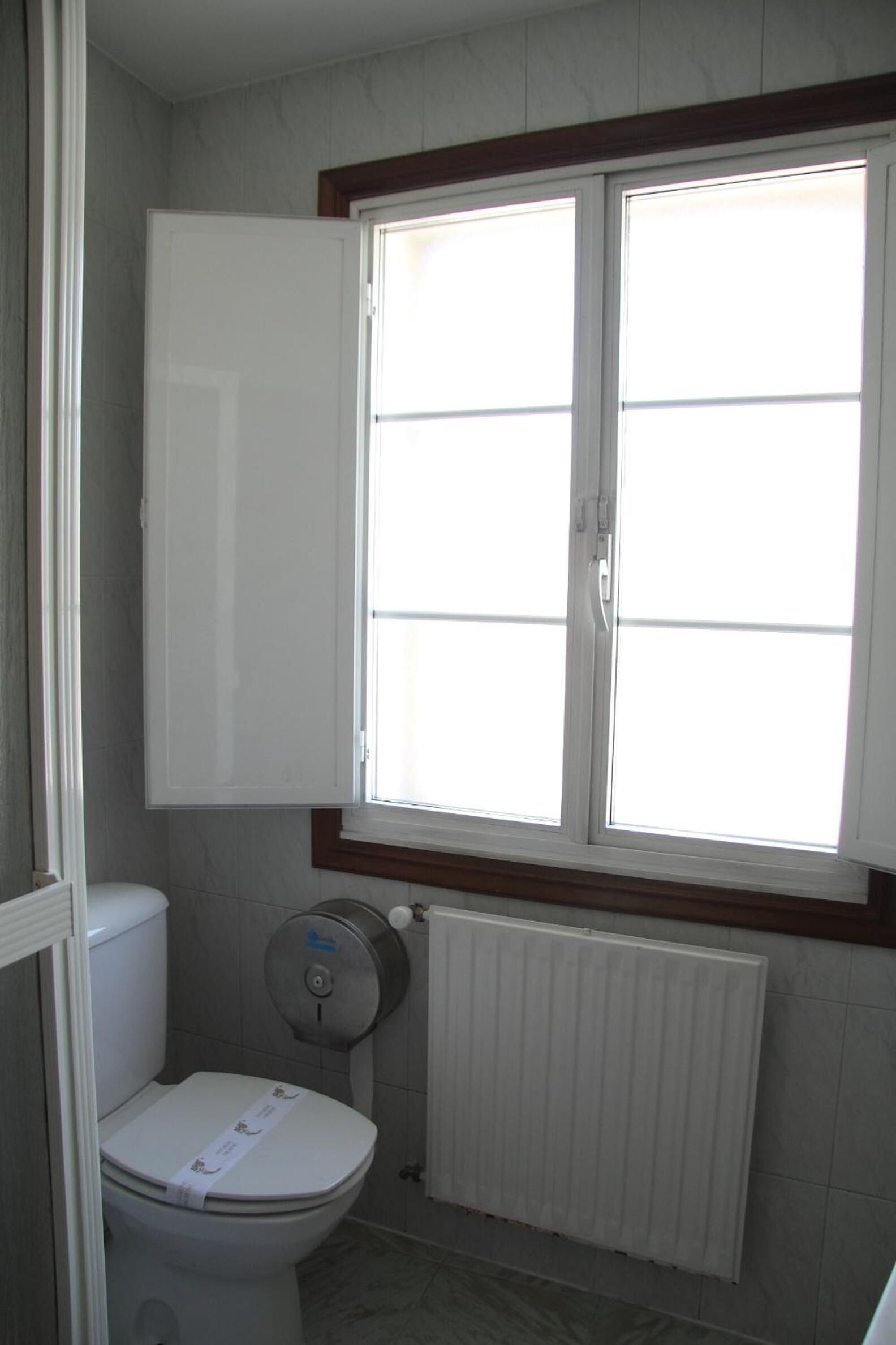 Een badkamer met een toilet, een raam en een radiator.