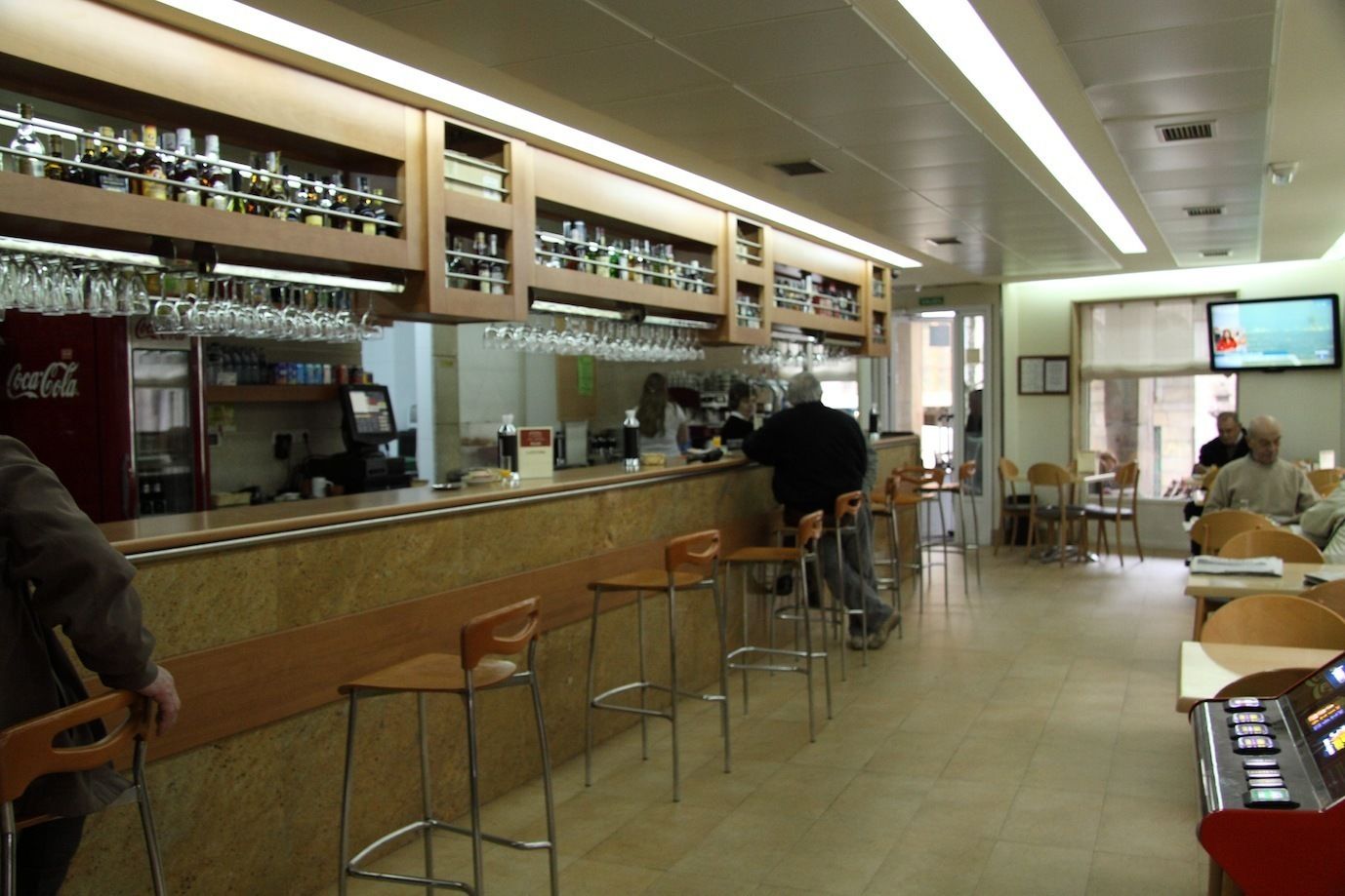 A bar area with stools, a counter, and shelves with bottles and glasses.