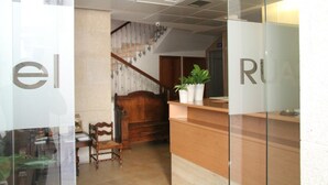 Zona de recepción con un mostrador de madera, una escalera y un área de estar con sillas.
