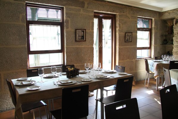 Un comedor con pared de piedra, ventanas amplias y una mesa dispuesta para cuatro.