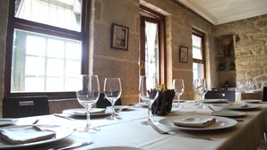 Mesa con vajilla, cubiertos y copas de vino en una habitación con paredes de piedra y ventanas amplias.