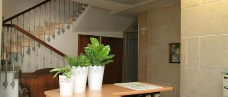 Una recepción con tres plantas en macetas, un mostrador de madera y una escalera con barandilla de metal.