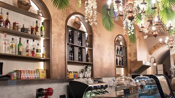A bar area with shelves of liquor bottles, a coffee machine, and a glass display case with pastries. - Odos Oneiron Hotel (Chania)