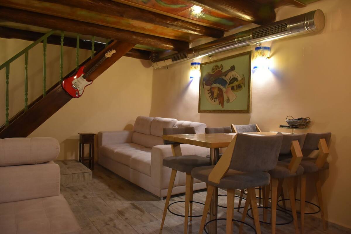 Un comedor con una mesa y sillas de madera, un sofá y una escalera con una guitarra apoyada.