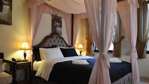 A four-poster canopy bed with a dark headboard, two bedside lamps, and a nightstand with a telephone. - Odos Oneiron Hotel (Chania)