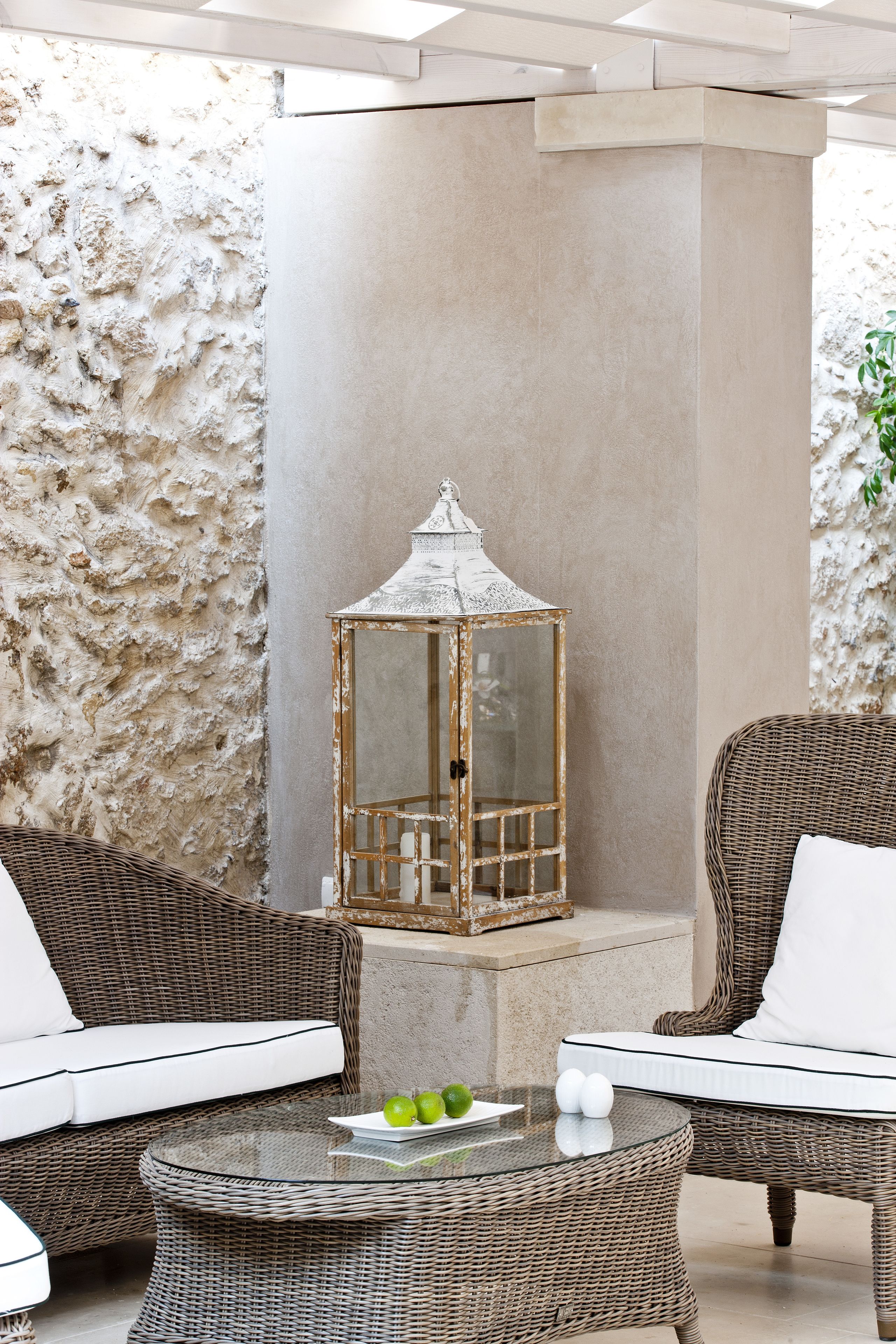 A wicker sofa with white cushions, a glass table with apples and eggs, and a decorative lantern.