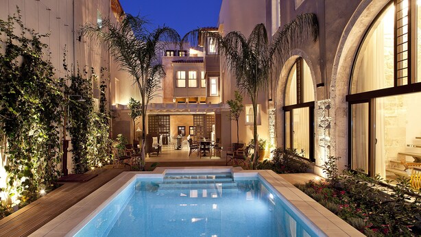 Ein Pool mit Fliesen umgeben von Pflanzen und einem Gebäude mit Bogenfenstern und einem Balkon.