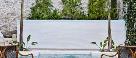 A pool area with two wicker chairs facing the water, surrounded by greenery and a stone wall.