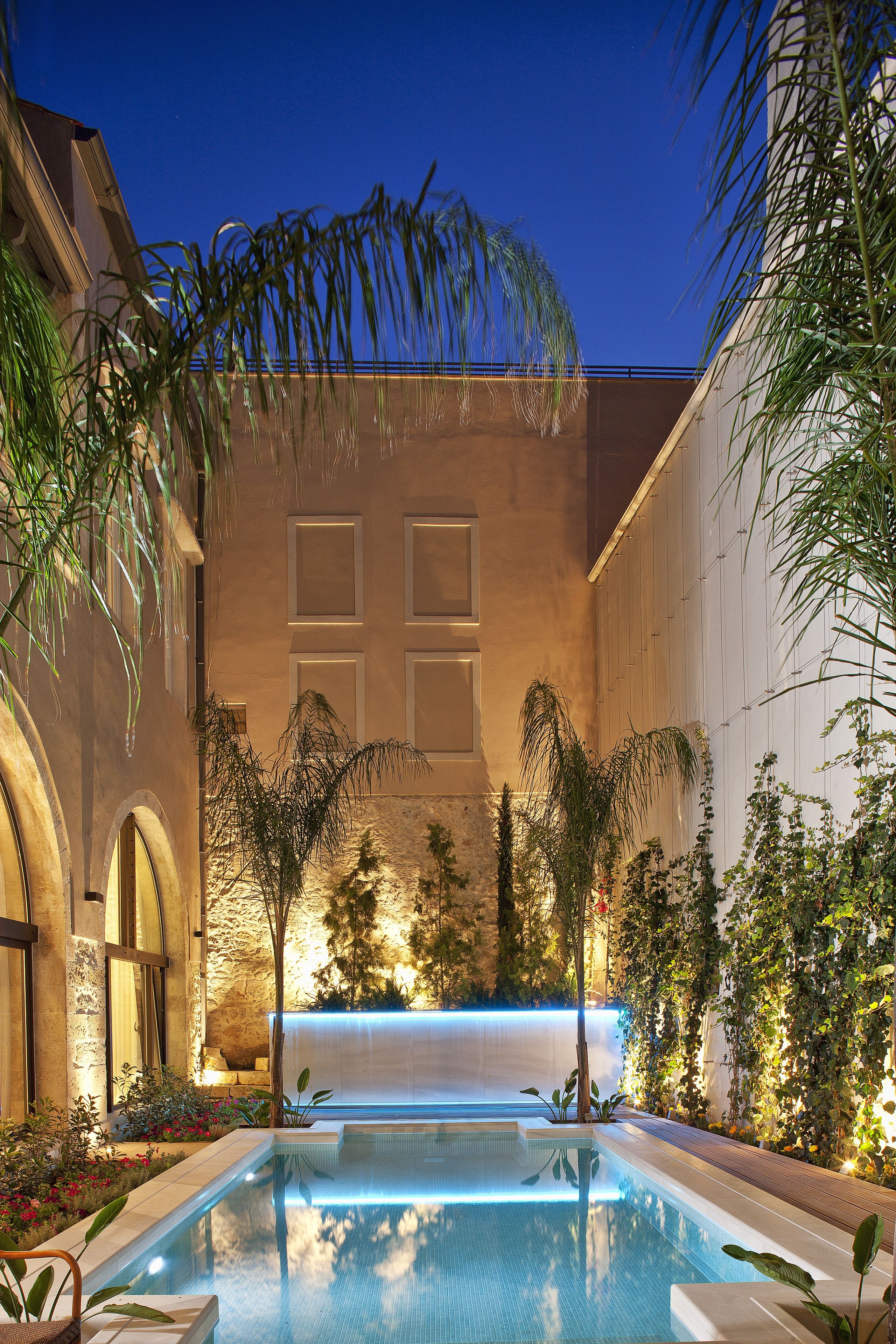 A swimming pool with a waterfall feature, surrounded by lush greenery and architectural elements.