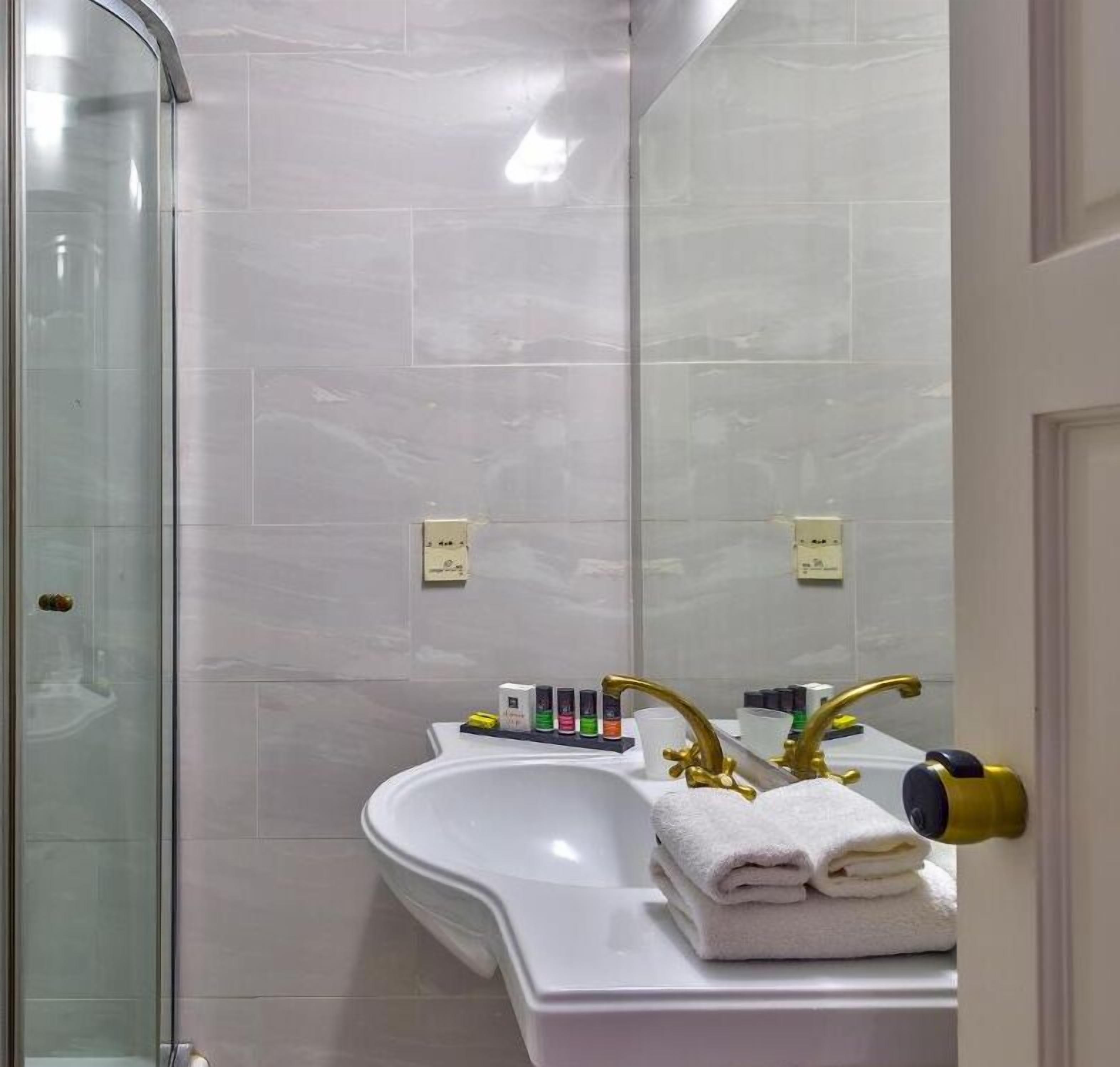 Ein Badezimmer mit Duschkabine aus Glas, einem weißen Waschbecken mit goldenen Armaturen und einem Spiegel.
