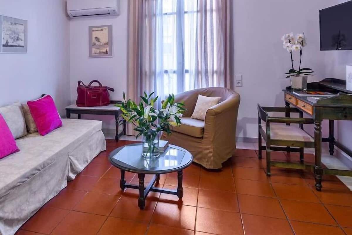 A cozy living room with a sofa, a chair, a small table with a vase of flowers, a TV, and a desk with a chair.