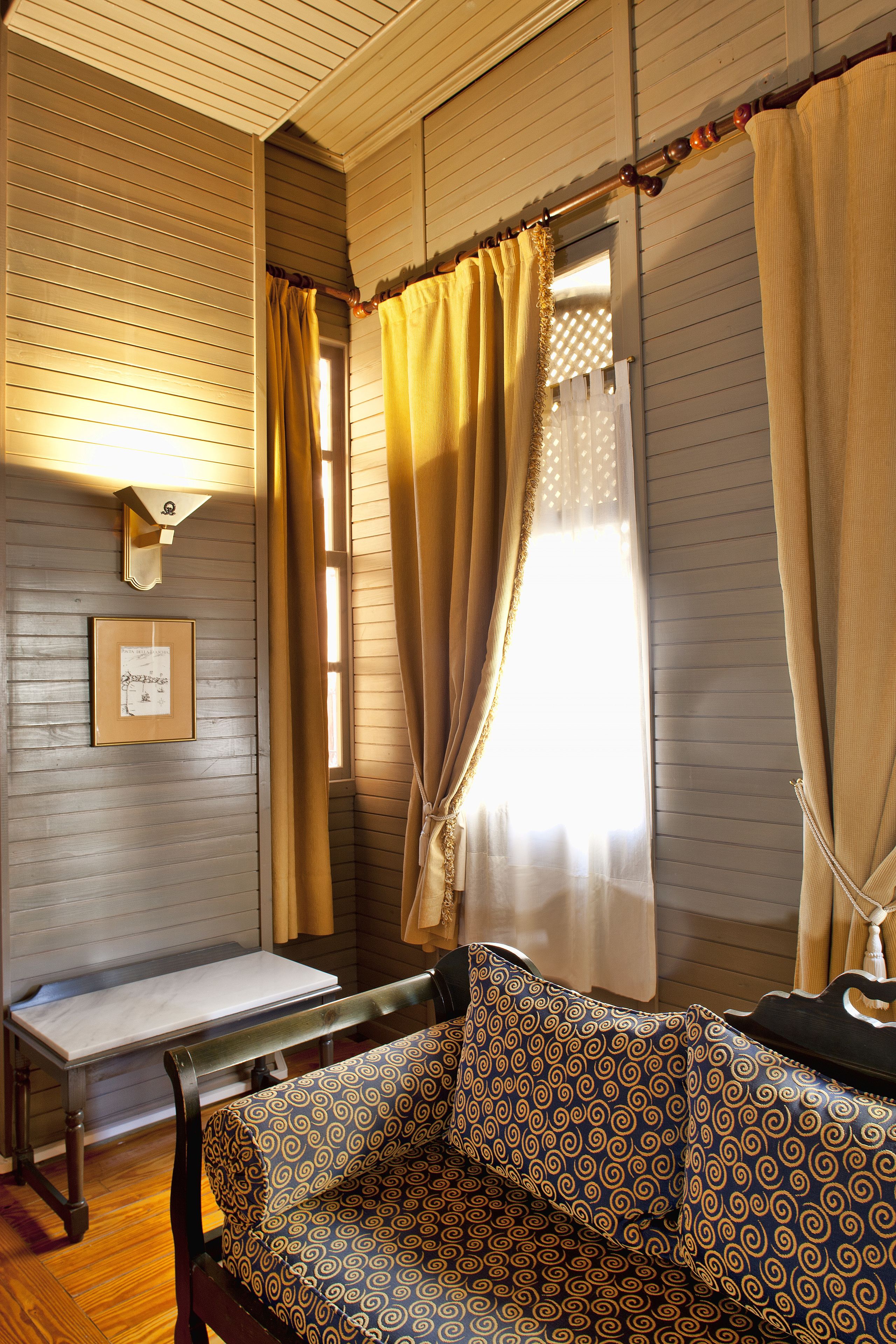 A room with wooden paneling, a bench, a patterned sofa, and a window with curtains.