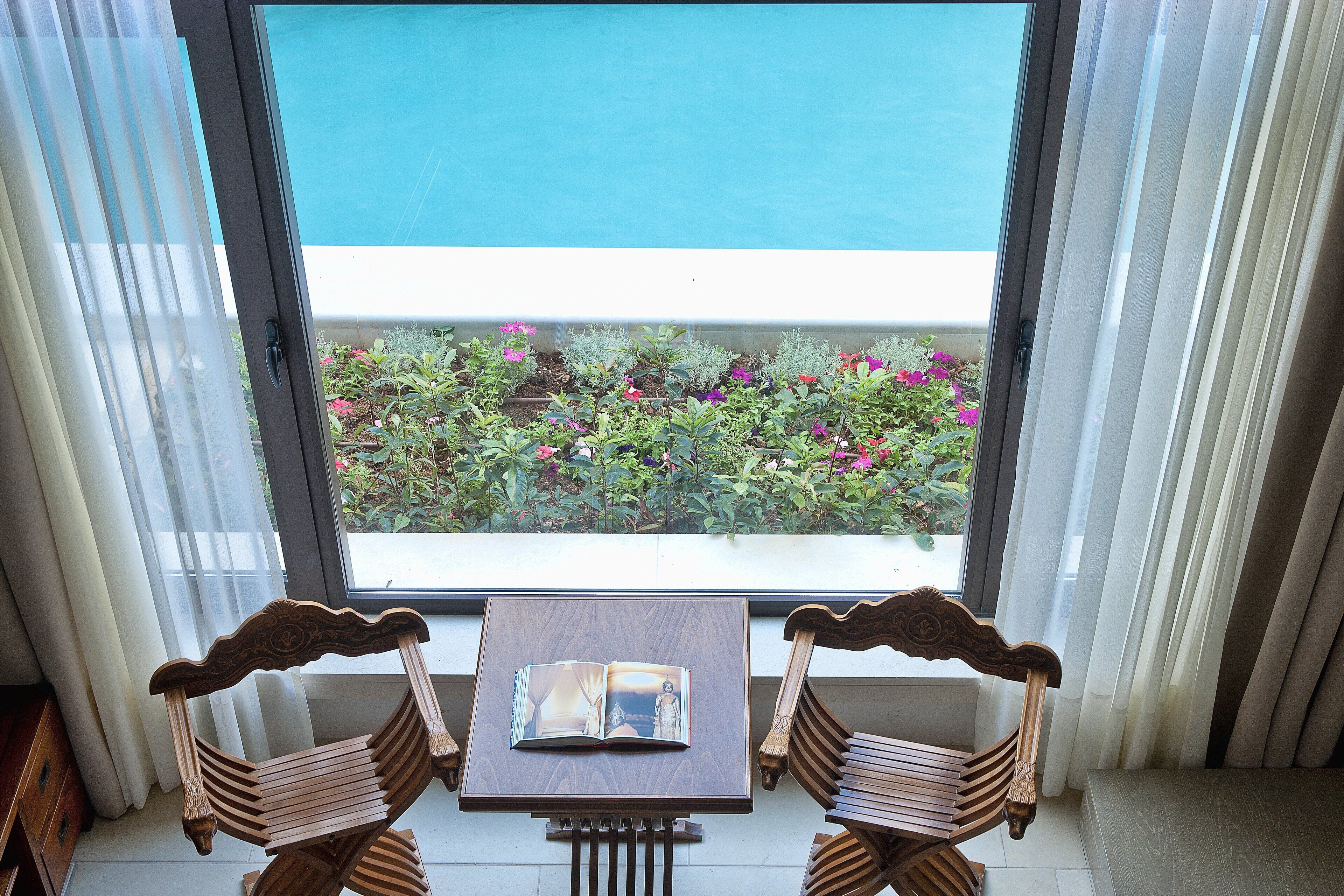 A balcony with a view of the sea, two wooden chairs, and a table with a book.