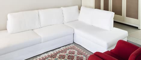 A white sectional sofa, a red armchair, a patterned rug, a framed painting, and a mirrored wardrobe.