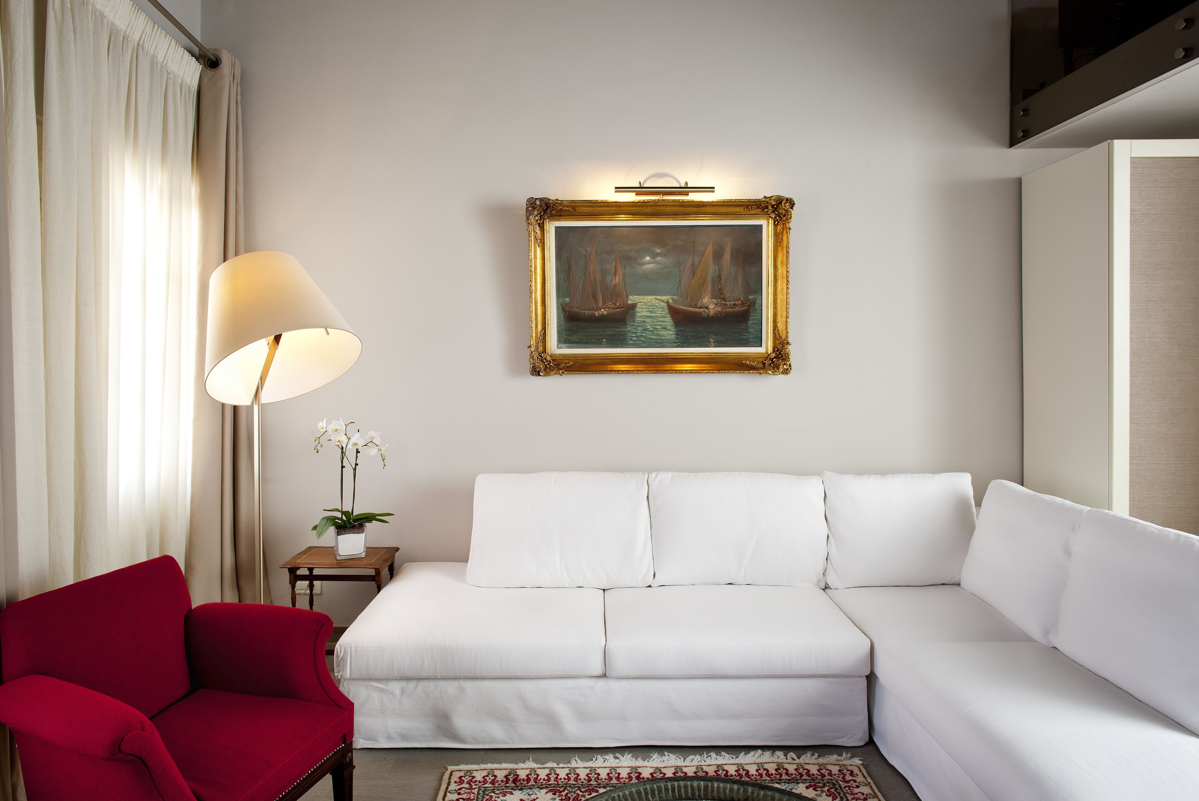 Ein weißes Sofa, ein roter Sessel, eine Lampe, ein gerahmtes Bild und ein kleiner Tisch mit einer Pflanze.