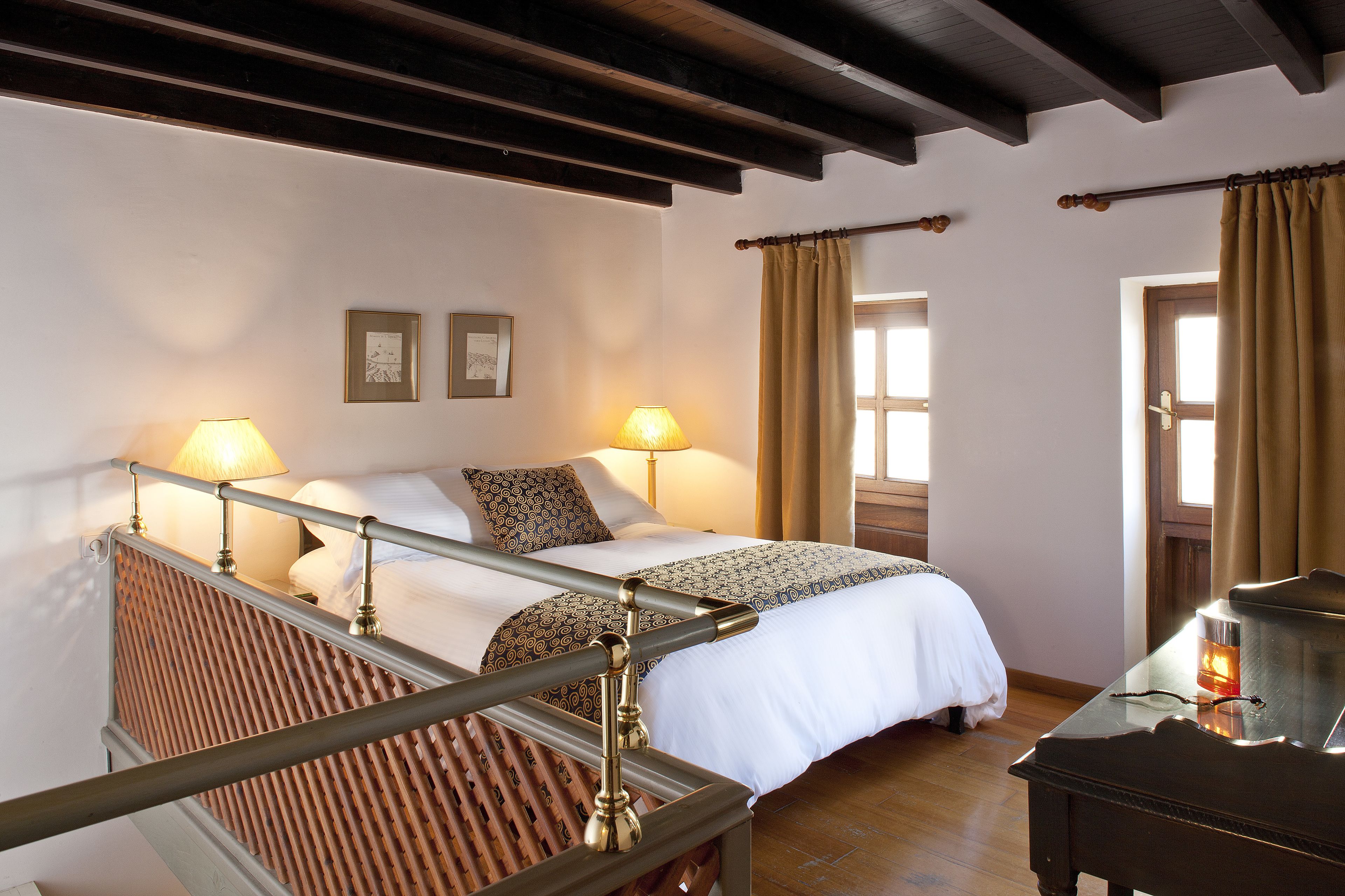 Een hotelkamer met een bed, twee bedlampen, een houten hoofdeinde, een piano en een raam met gordijnen.
