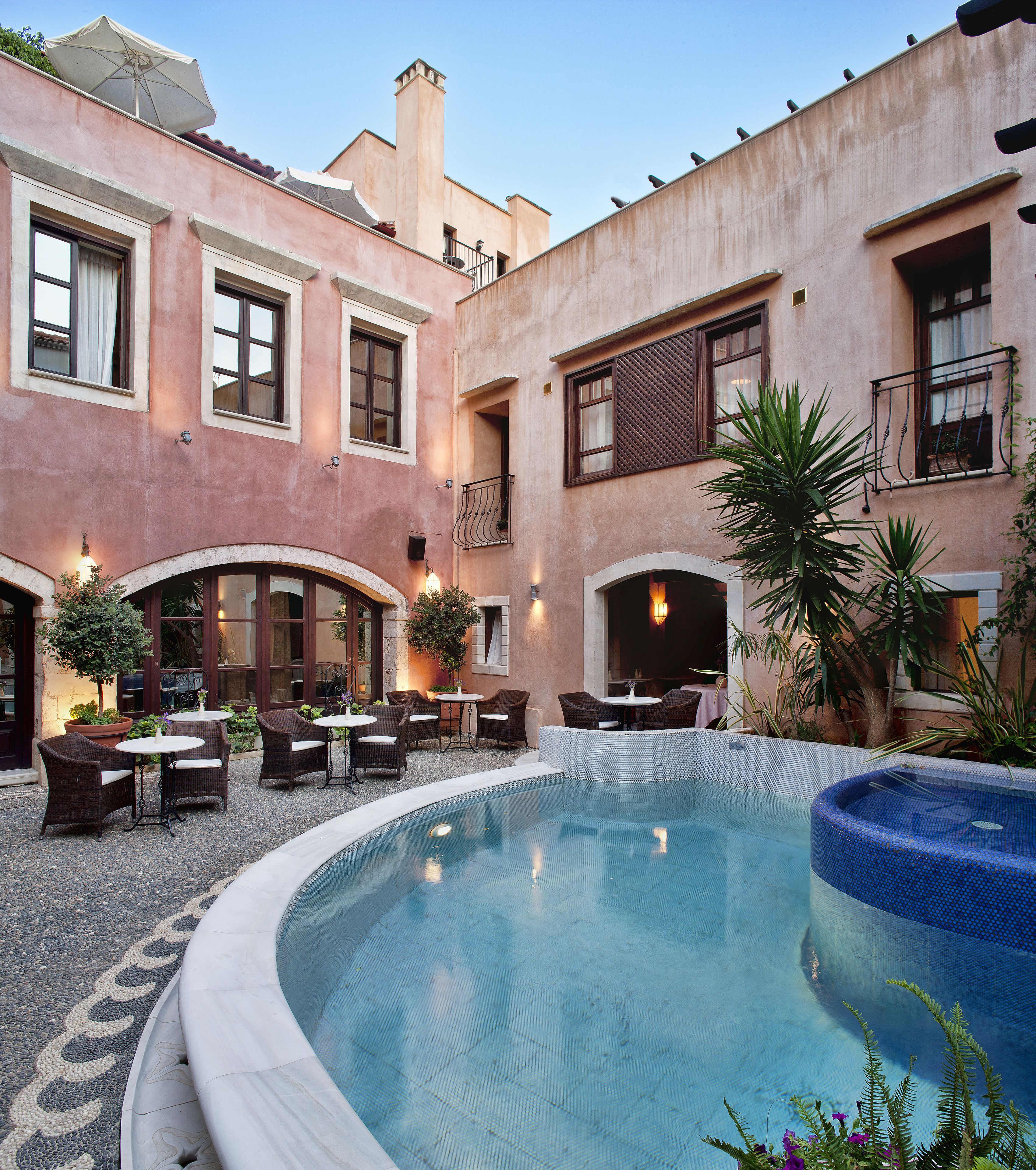 Un patio con piscina, mobiliario exterior y un edificio con varias ventanas y balcones.
