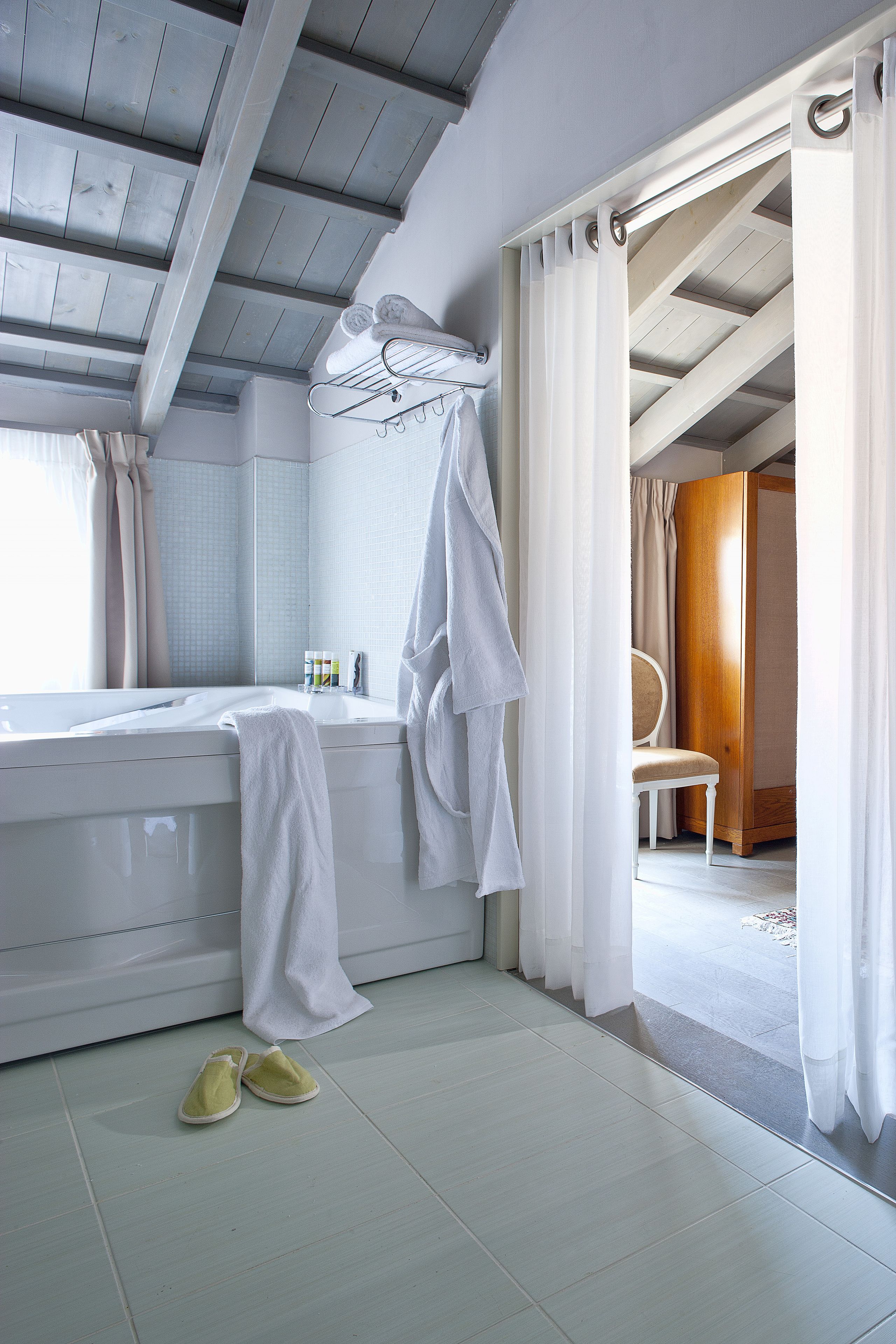 Ein Badezimmer mit Badewanne, einem Sessel und einem Paar Hausschuhen auf dem Boden.