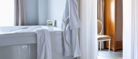 Un baño con bañera, una silla y un par de pantuflas en el suelo.