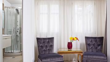 A bathroom with a glass shower enclosure, a vanity, and a window with sheer curtains.