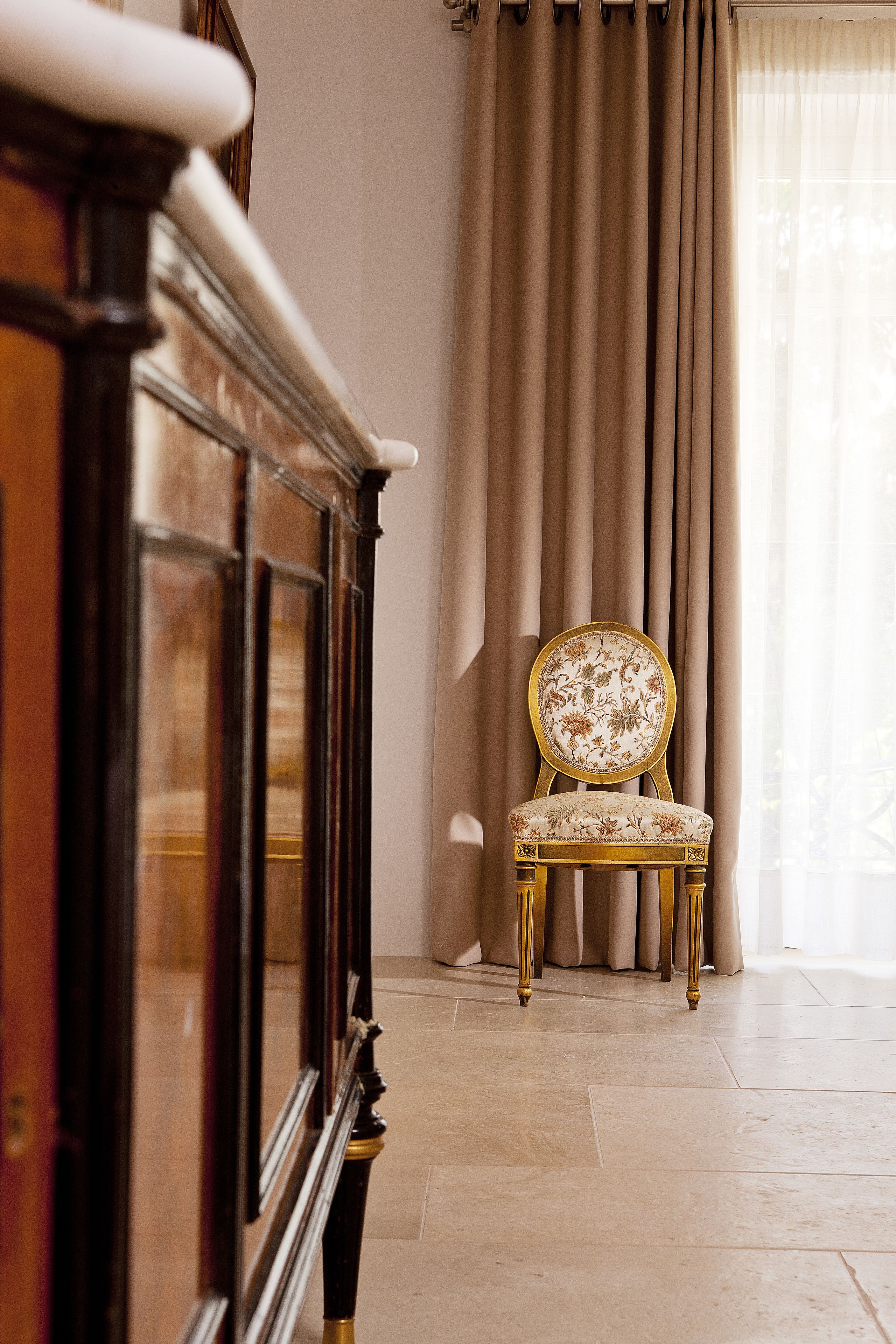 A room with a piano, a chair with floral upholstery, and a large window with curtains.