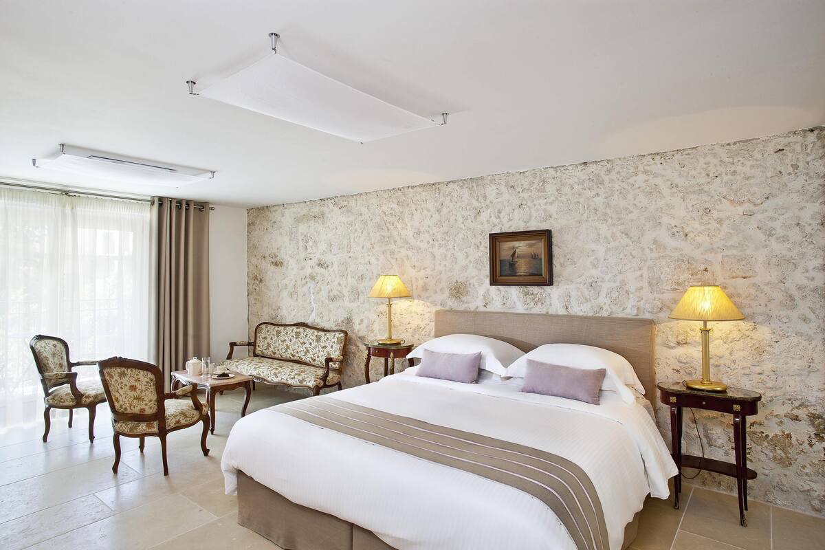 A hotel room with a large bed, two bedside tables with lamps, a chair, a small table, and a sofa.
