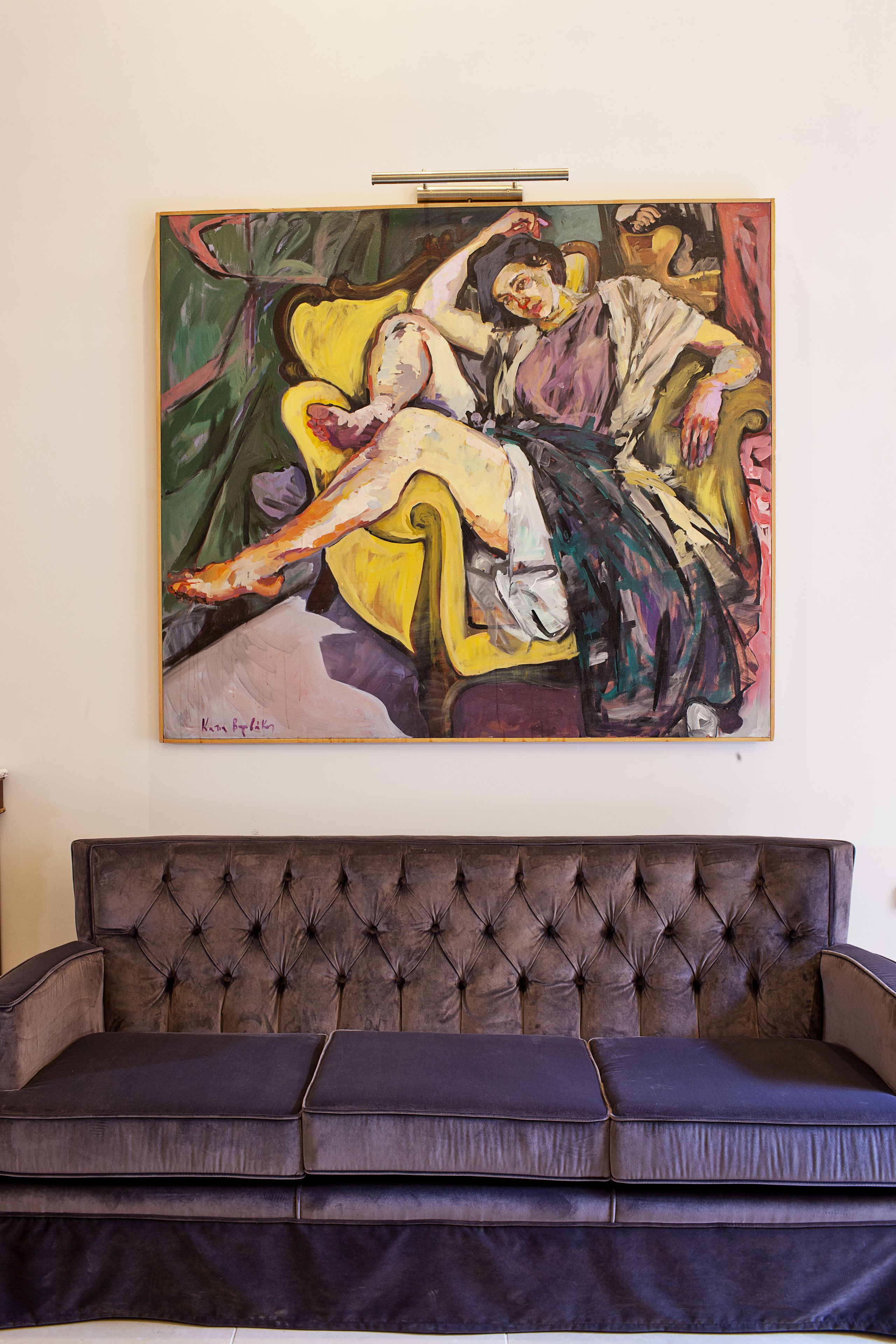 A room with a large painting on the wall, a tufted headboard, and a dark-colored sofa.