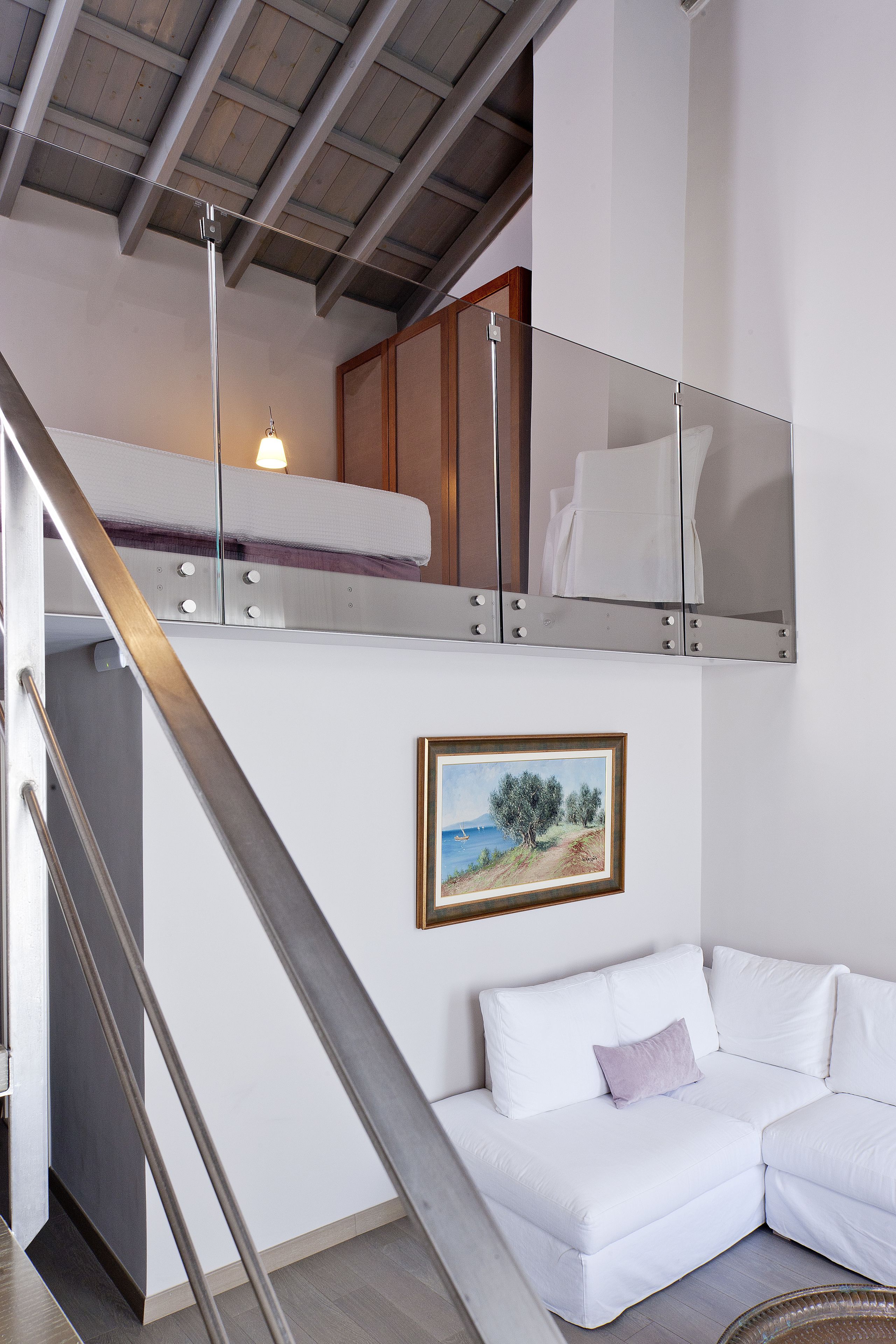 Un interior moderno con un sofá blanco, un cuadro de un paisaje y una cama litera con cabecera de madera.