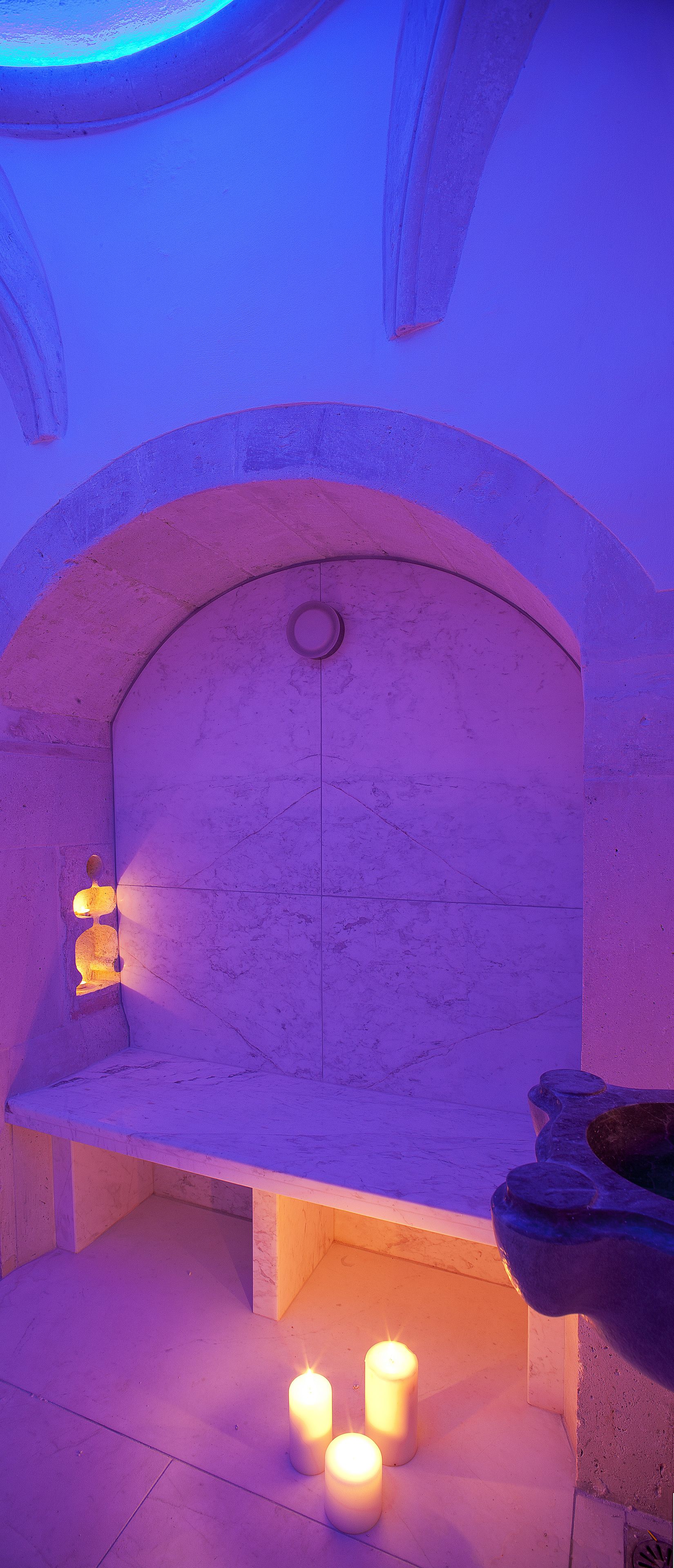 A stone bench with a candle holder and candles in a room with a stone wall and ceiling.