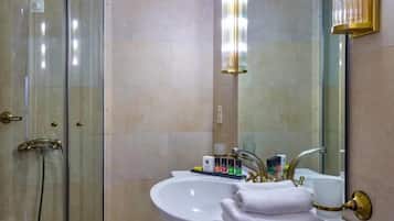 A bathroom with a glass-enclosed shower, a white sink with gold fixtures, and a large mirror.