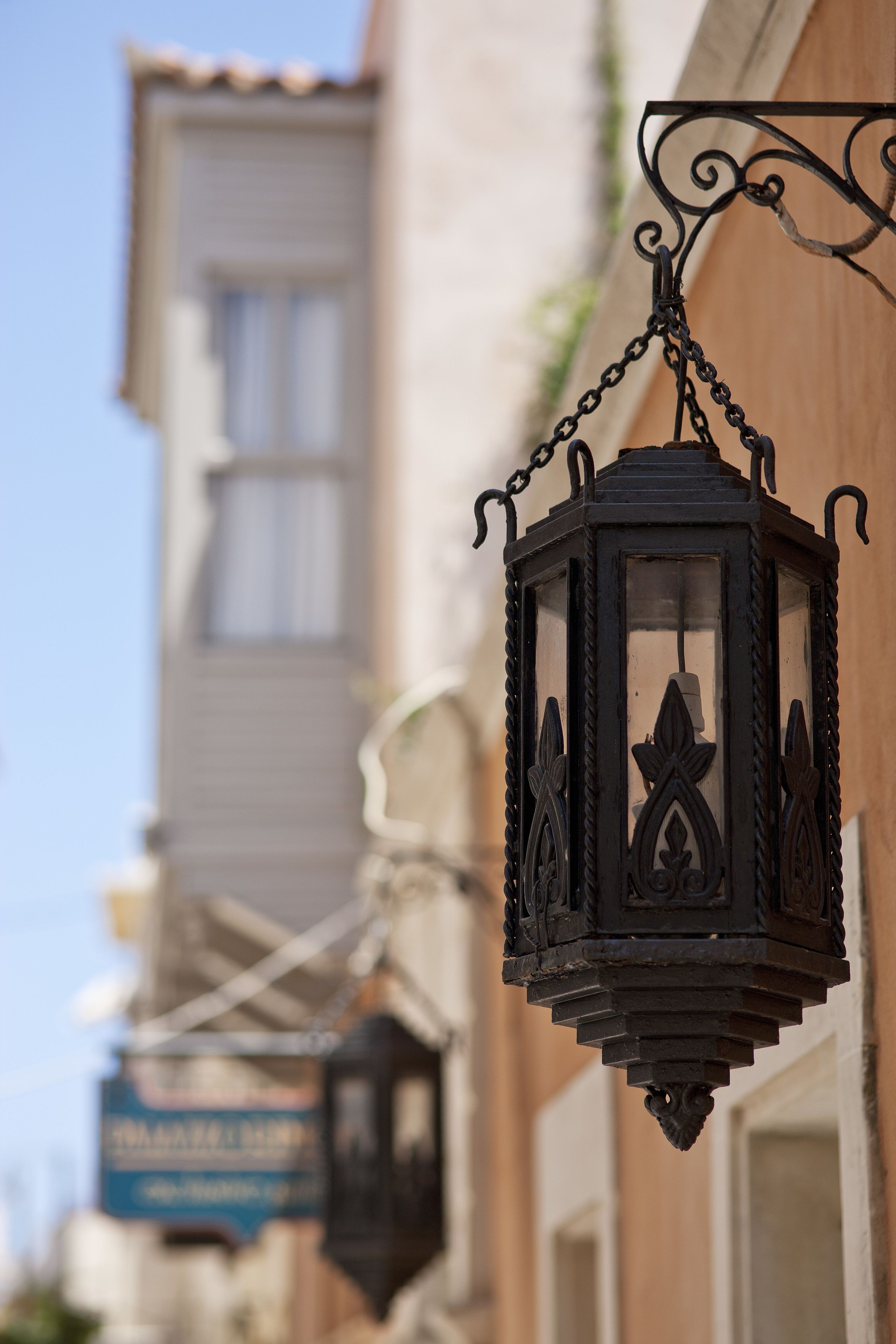 A hanging black lantern with intricate designs, attached to a building with a visible sign and windows.