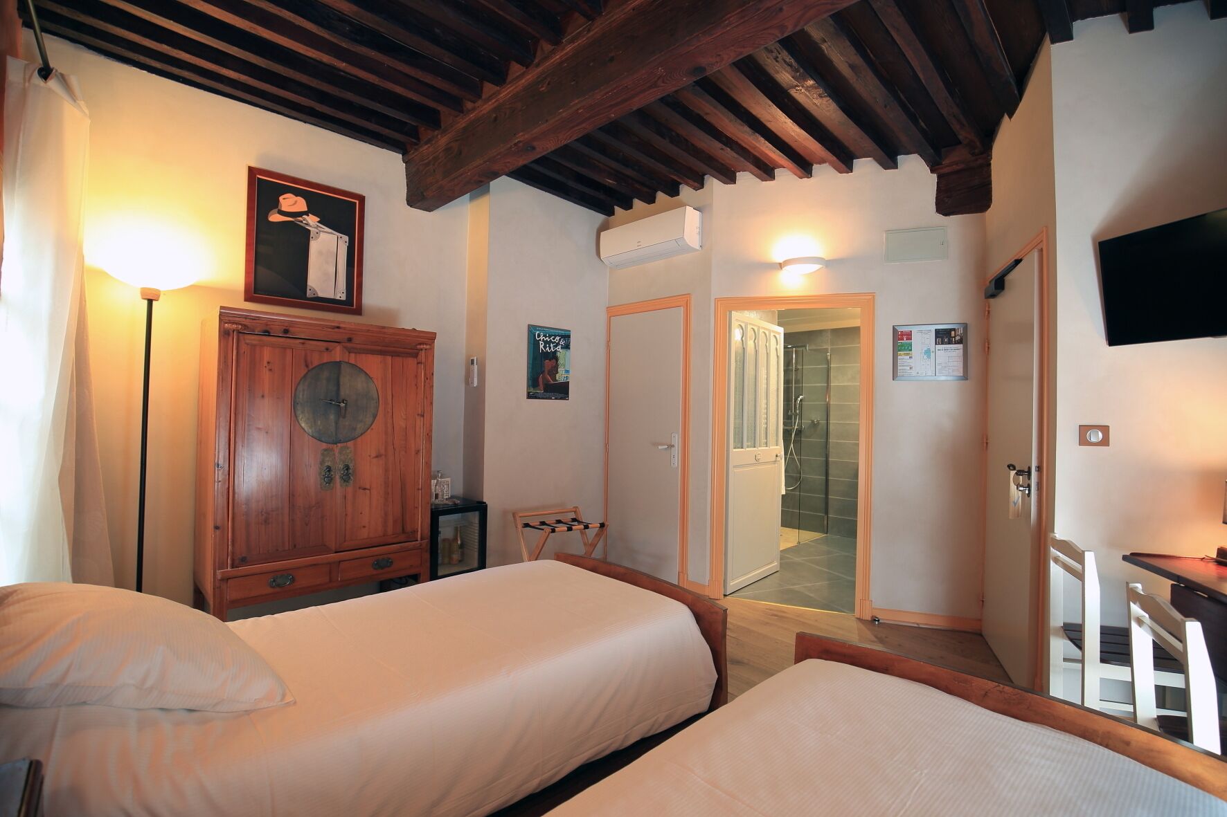 A bedroom with two beds, a wooden wardrobe, a small table, a chair, and a shower room.