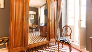 Una habitación con un armario grande de madera, una alfombra estampada, una silla y una puerta que da a otra estancia.