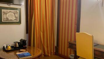 A room with a round wooden table, a yellow chair, a framed map, a television, and striped curtains.