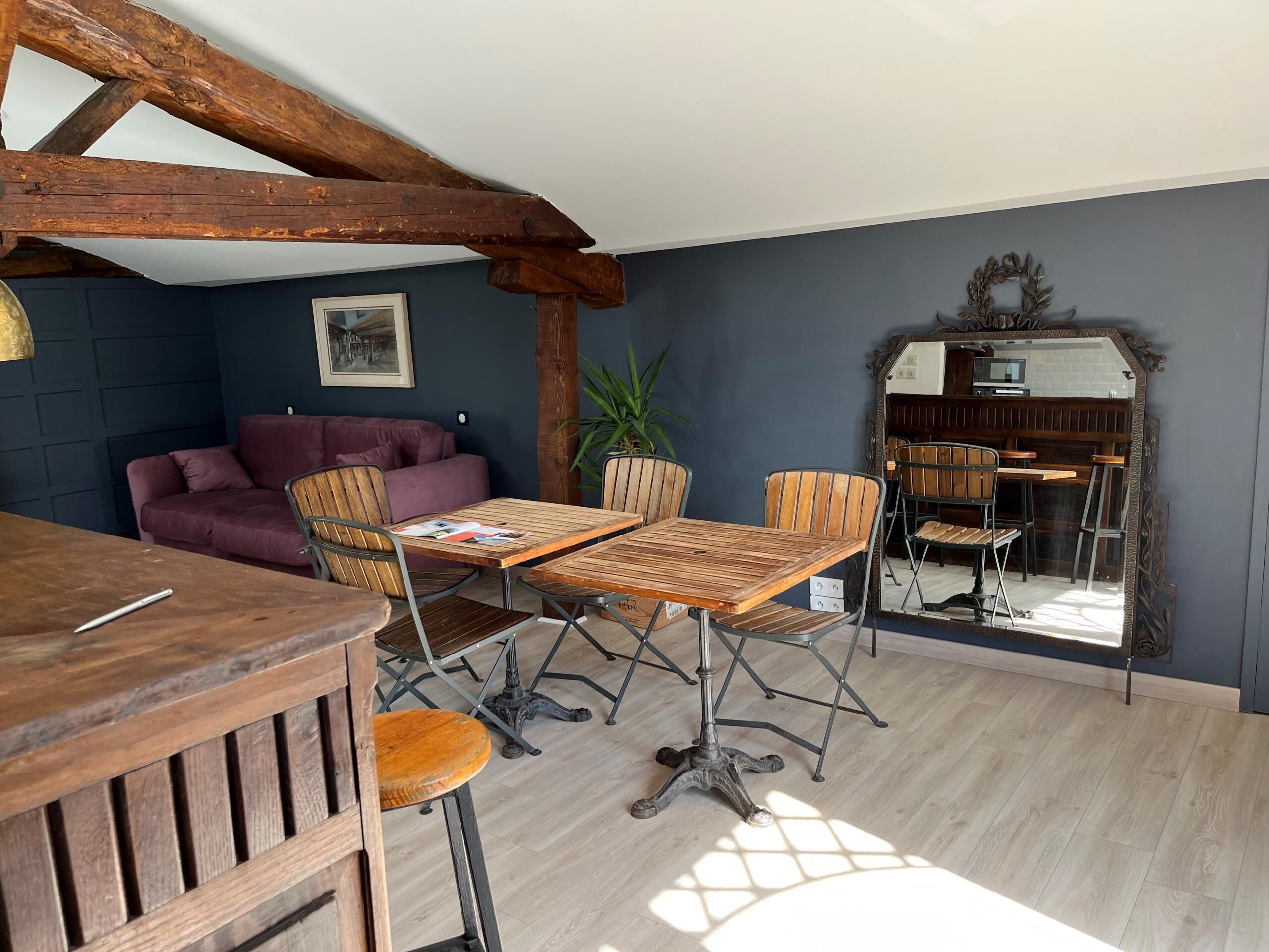 A dining area with a wooden table and chairs, a sofa, and a mirror reflecting the room.