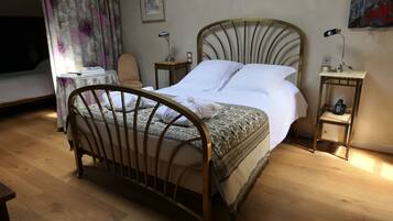 A neatly made bed with a metal frame, a bedside table with a lamp, and a small bedside table with a phone.