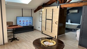 Un salón moderno con una mesa de madera, un televisor que muestra canales deportivos y un tragaluz.