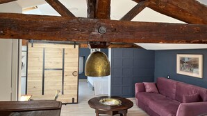 Una habitación rústica con vigas de madera a la vista, una puerta de madera, un sofá morado y una mesa redonda de madera con una bandeja de latón.