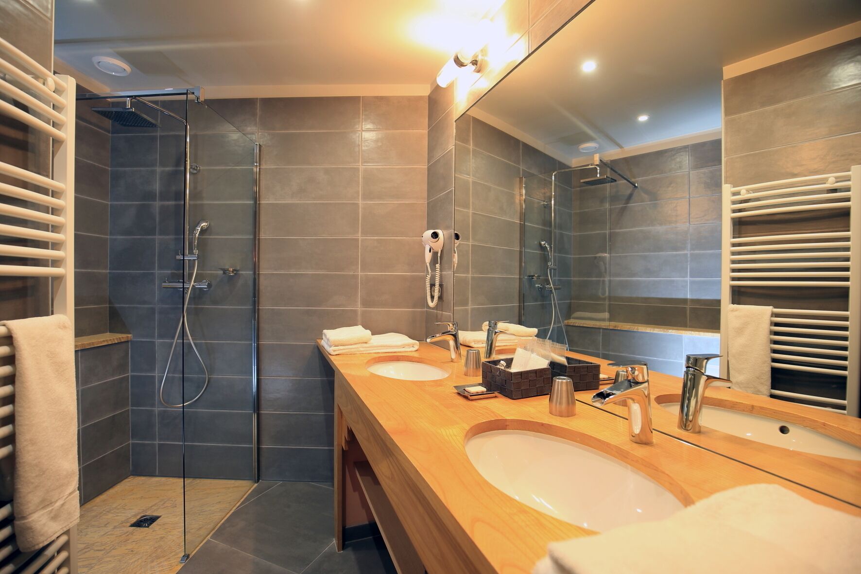 Een moderne badkamer met twee wastafels, een douchecabine met glazen wanden en een grote spiegel.