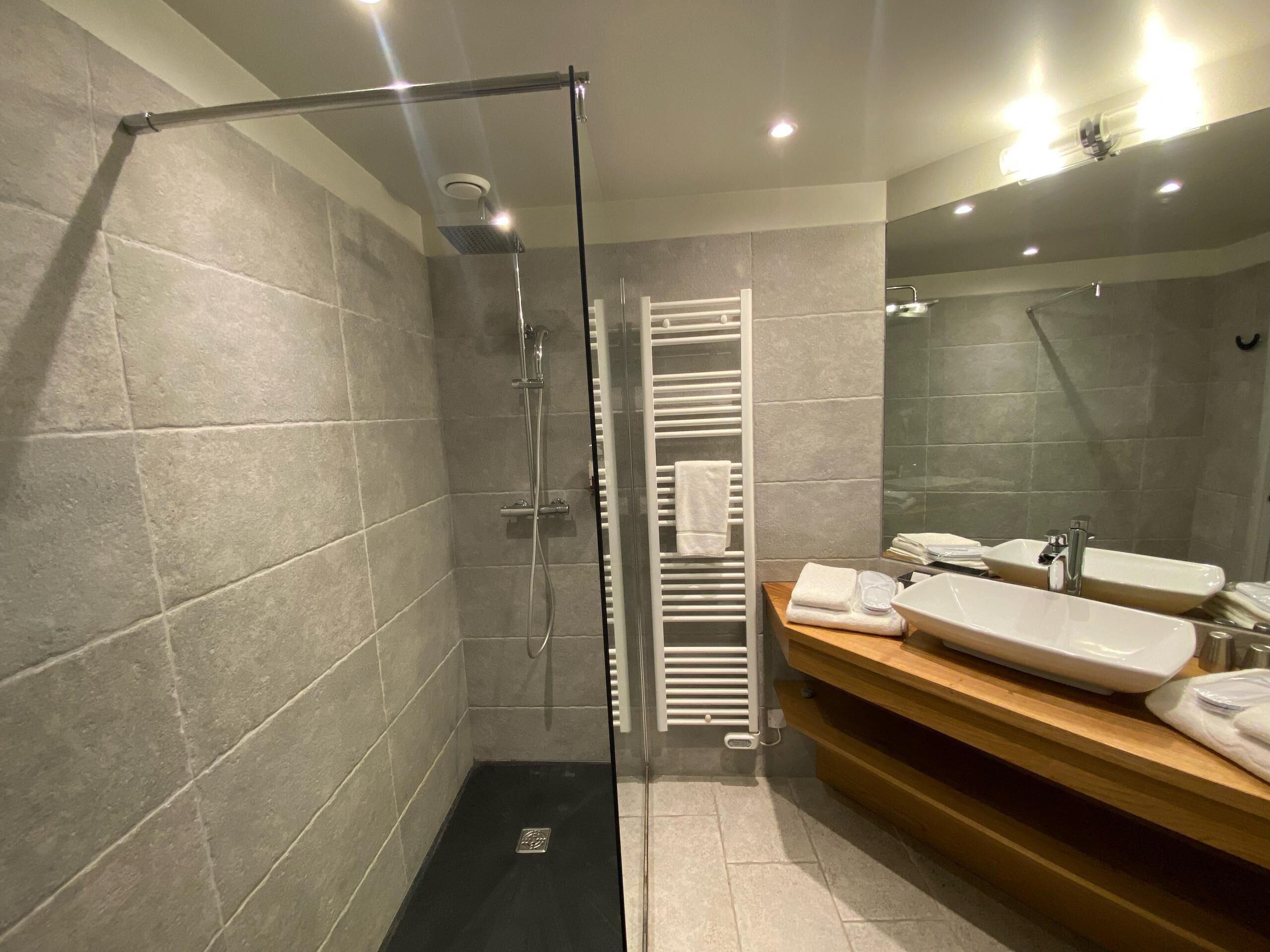 Un baño moderno con ducha envuelta en vidrio, tocador de madera con dos lavamanos y un perchero para toallas.