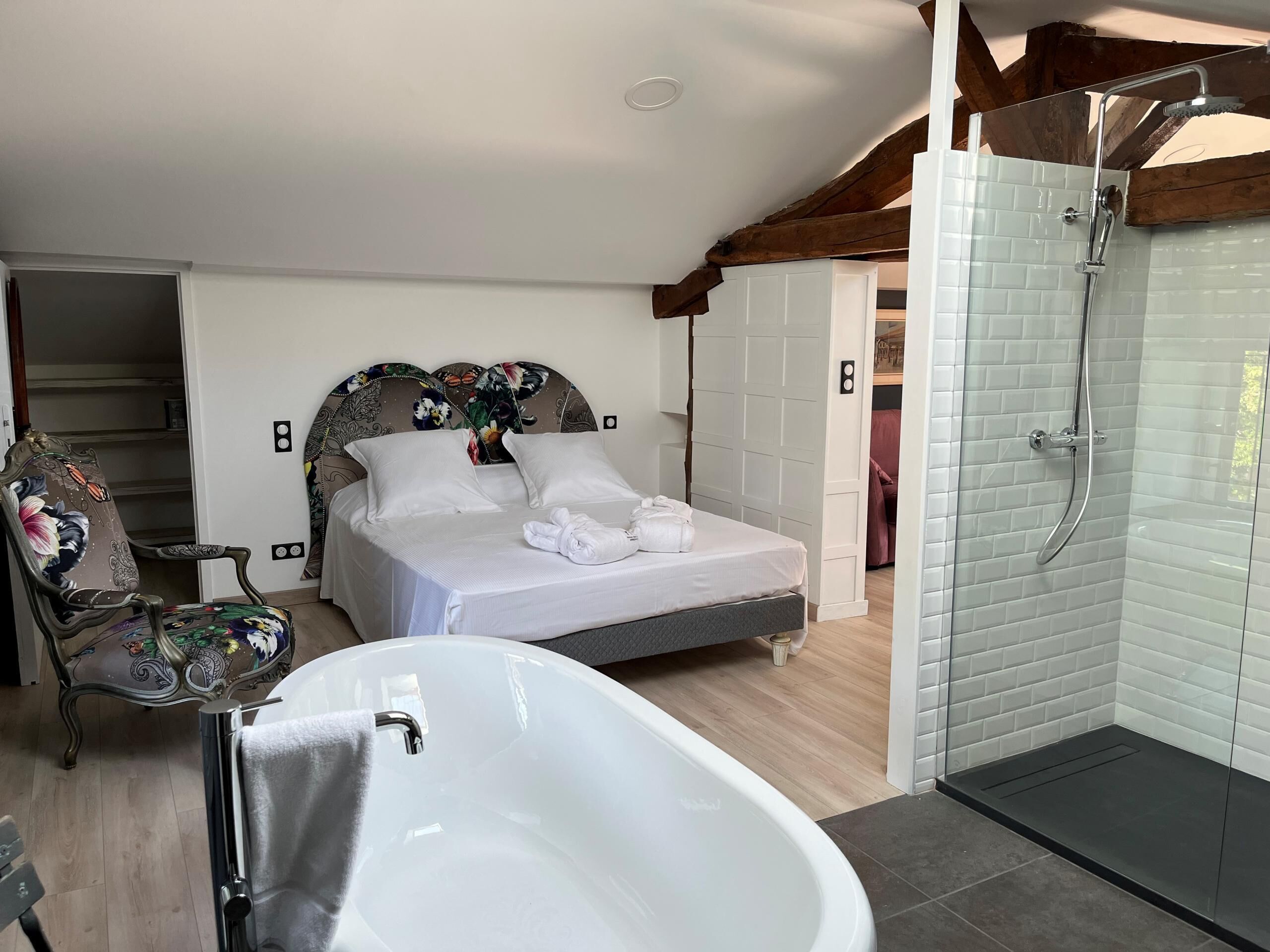 A bedroom with a bed, a chair, a bathtub, and a shower area.