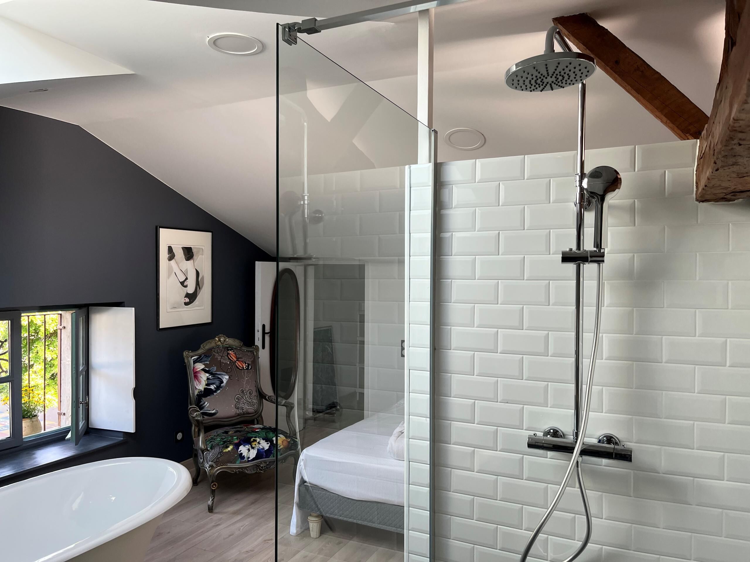 A modern bathroom with a glass shower enclosure, a freestanding bathtub, and a wooden-framed window.